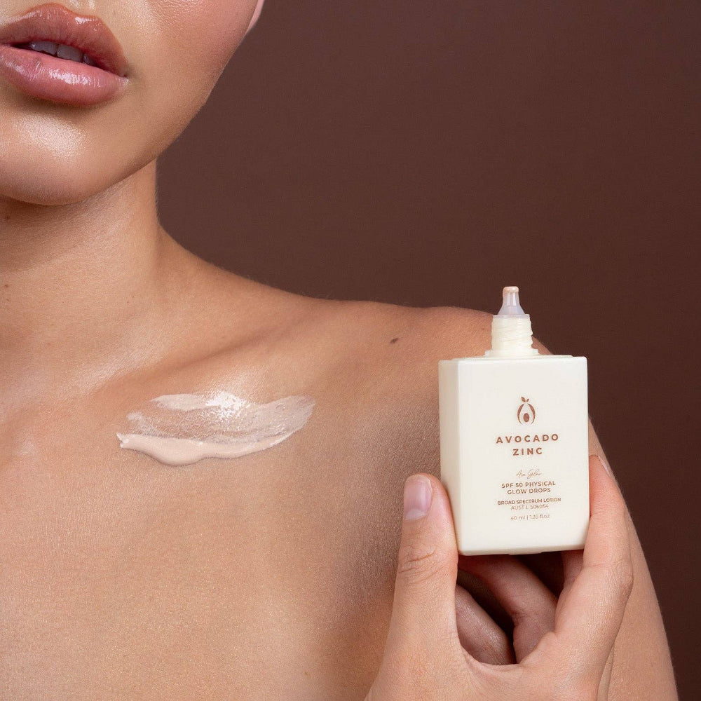 Person applying Avocado Zinc skincare product to shoulder with a brown background